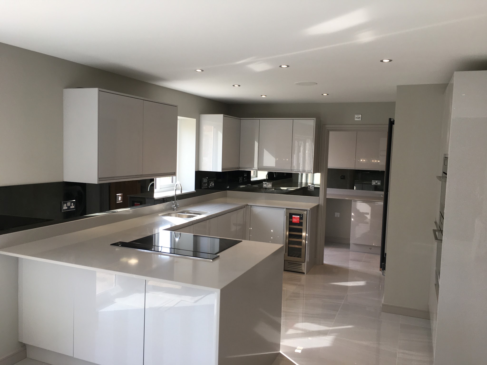 White and grey gloss L-shaped kitchen with black glass splashback