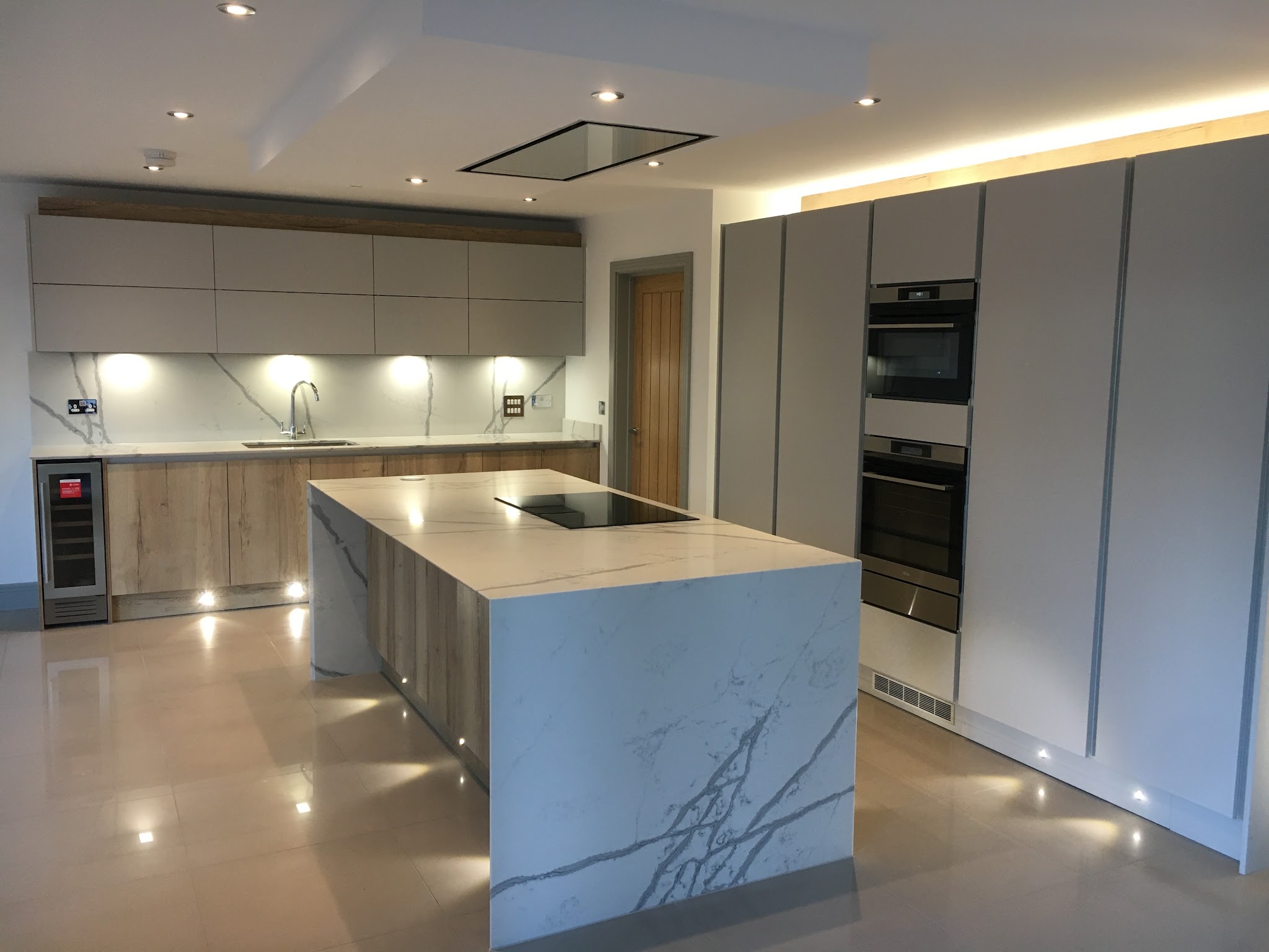 Handleless grey kitchen with oak-effect tall units and a marble-look waterfall island, fitted by Mike Ross