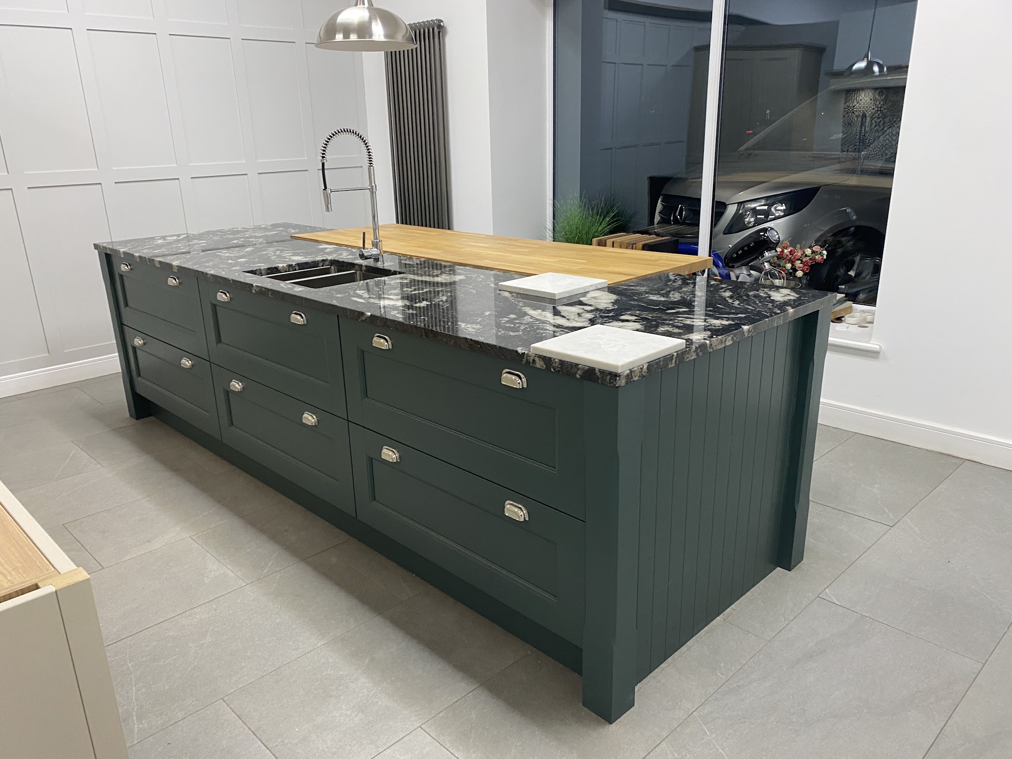 Dark green shaker island with a dark stone top and a solid wood block