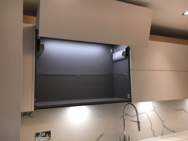 Lift-up wall cabinet with interior lighting over a marble-look splashback